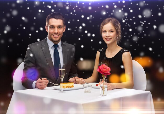 Concetto di cibo, natale, vacanze e persone - coppia sorridente che mangia dessert al ristorante su sfondo di luci notturne