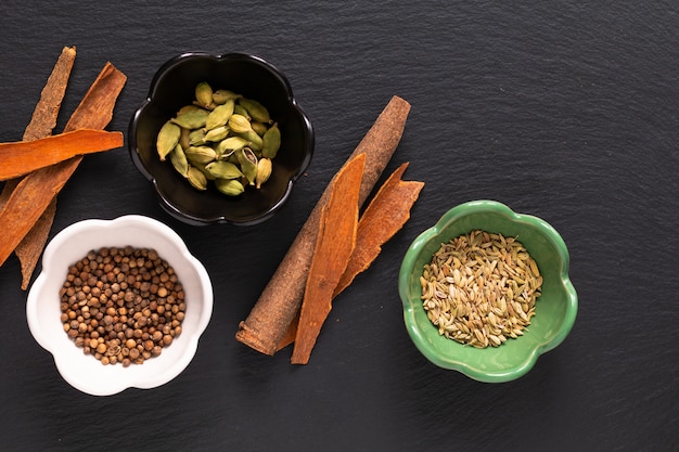 Food concept assortment Oriental spices cardamom pods, coriander seeds, fennel and Cinnamon Cassia Bark Sticks on black slate 