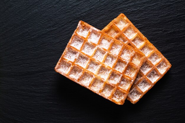 Photo food concept classic square waffles with icing sugat toping on black slate stone board