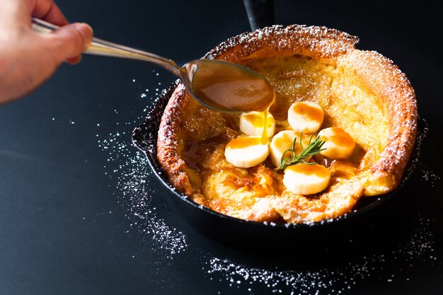 Food concept Homemade Dutch baby or German  banana caramel topping pancake in skillet iron cast on black