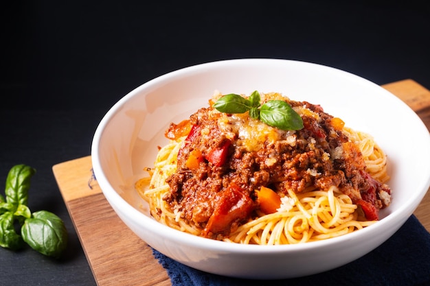 Foto concetto di cibo spaghetti biologici fatti in casa alla bolognese in ciotola di pasta su tavola di legno con sfondo nero e spazio per la copia