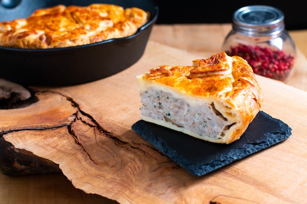 Food concept homemade pork pie or meat pie on stone plate and cast iron skillet on wooden background