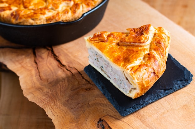 Food concept homemade pork pie or meat pie on stone plate and cast iron skillet on wooden background