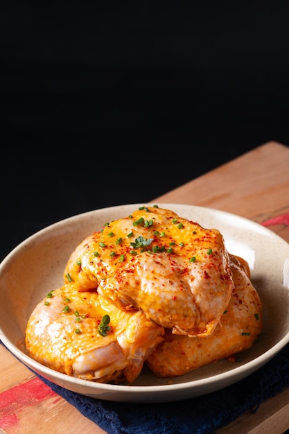 Concetto di cibo marinata piccante fatta in casa di cosce di pollo in ciotola di ceramica su tavola di legno con sfondo nero e spazio per la copia