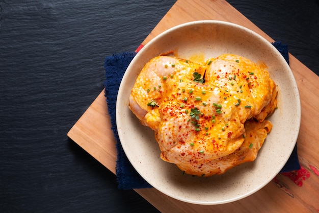 Food concept homemade spicy chicken thighs marinade in ceramic bowl on wooden board with black background and copy space