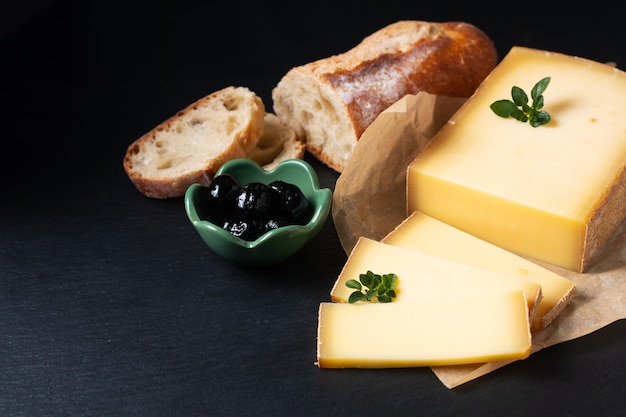 Food concept organic French Comte cheese with french bread baquette on black slate stone board with copy space