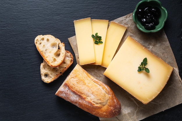 Food concept organic French Comte cheese with french bread baquette on black slate stone board with copy space