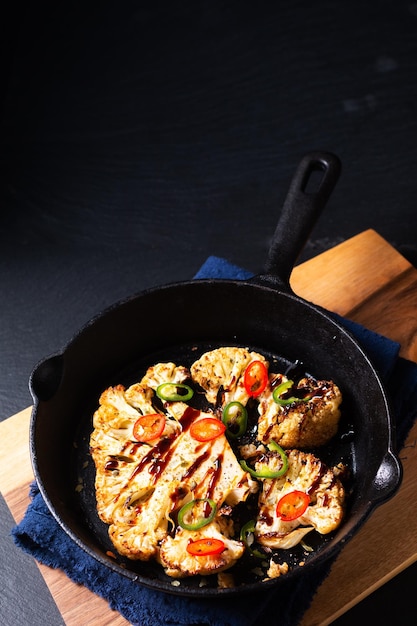 Food concept Roasted organic Cauliflower in skillet iron pan on black slate stone background with copy space