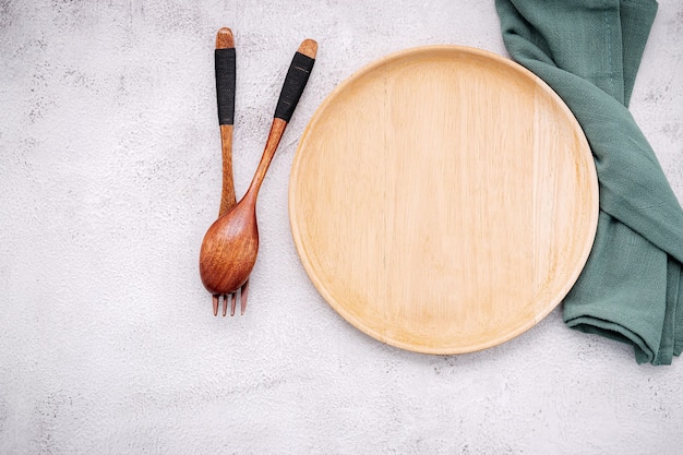 Food conceptual image of wooden plate with spoon and fork on white concrete.