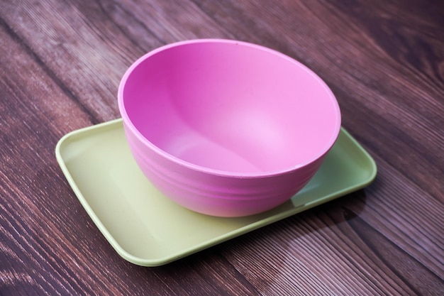 Food containers made of plastic include bowls plates and square plates in pink and green on wood