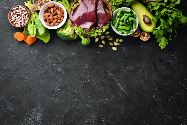 Food containing natural iron Fe Liver avocado broccoli spinach parsley beans nuts on a black stone background Top view