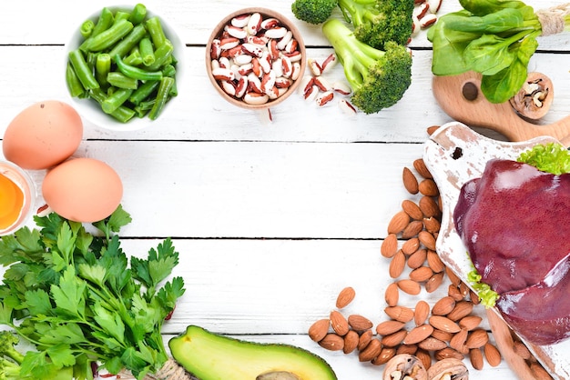 Foto alimenti contenenti ferro naturale fe fegato avocado broccoli spinaci fagioli prezzemolo noci su fondo di legno bianco vista dall'alto