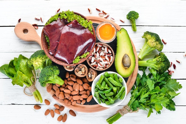 Food containing natural iron Fe Liver avocado broccoli spinach parsley beans nuts on a white wooden background Top view