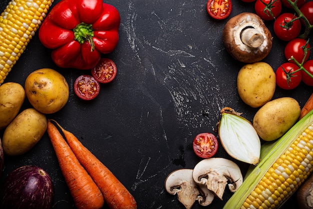 Food cooking background with ingredients, assorted raw fresh uncooked vegetables on black dark stone background from above