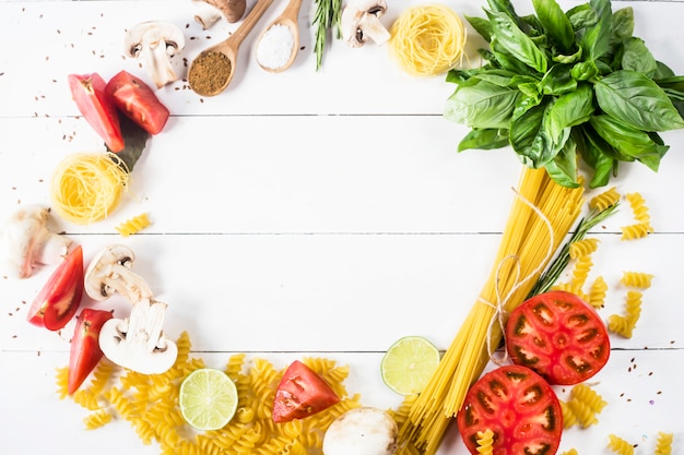 Food for cooking - pasta, basil, vegetables, lime and spices on a white wooden table