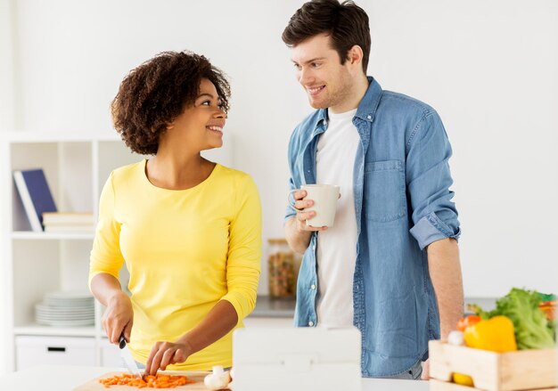 food, cooking, people, international and healthy eating concept - happy couple with tablet pc computer chopping vegetables and talking at home kitchen