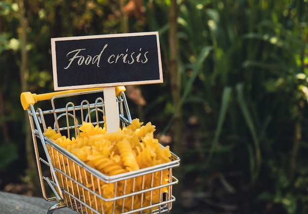칠판 라벨의 FOOD CRISIS 텍스트 농업 배경에 파스타로 채워진 쇼핑 트롤리 카트 식품 및 식료품 쇼핑 가격 인상 식품 가격 상승 식품 위기 인플레이션