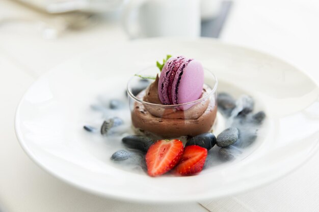 food, culinary, haute cuisine and cooking concept - close up of chocolate dessert with macaron cookie and fresh strawberry at restaurant