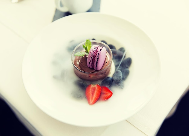 food, culinary, haute cuisine and cooking concept - close up of chocolate dessert with macaron cookie and fresh strawberry at restaurant