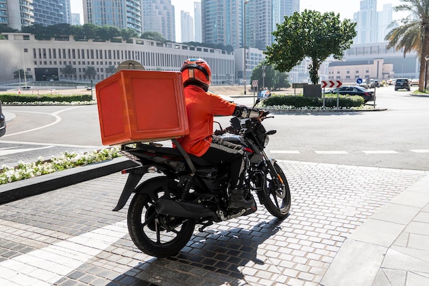 Photo a food delivery courier is driving an order to a customer's home on a moped takeaway food during quarantine transport delivery of parcels at home motorcycle rider with a big backpack