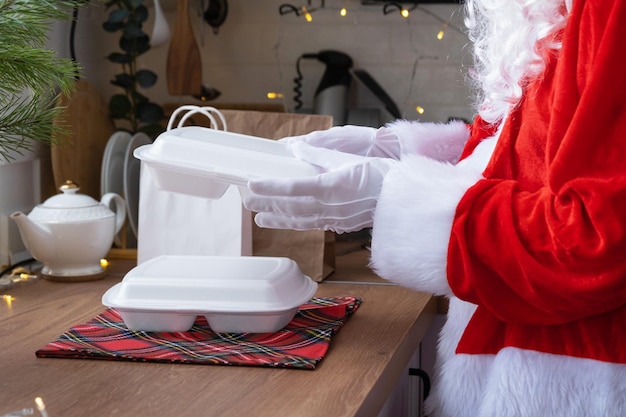 Food delivery to home service containers in hands of Santa Claus puts it on kitchen table and takes it away Readymade hot order Christmas New year holidays catering