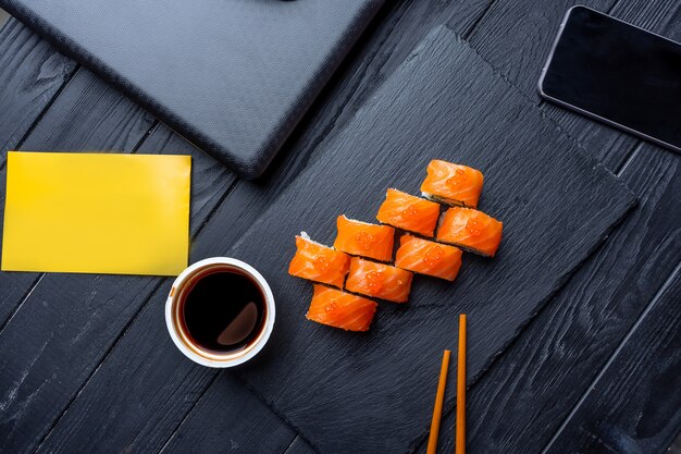 Photo food delivery to the office. set of sushi with salmon surrounded by office accessories: laptop, phone. office healthy snack