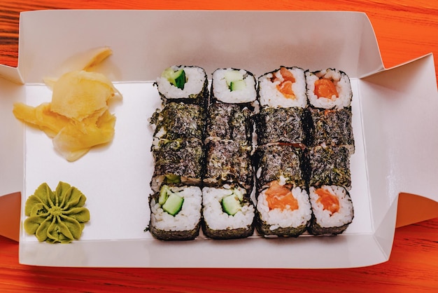 Food delivery rolls in a box on an orange background Japanese food rolls with salmon and cucumber