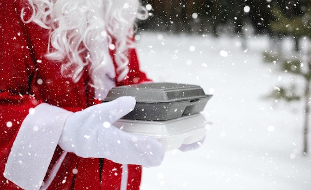 雪の中で屋外のサンタ クロースの手に食品配達サービス コンテナー クリスマス イブ プロモーション既製ホット オーダー使い捨てプラスチック ボックス年末年始ケータリング コピー スペース モックアップ