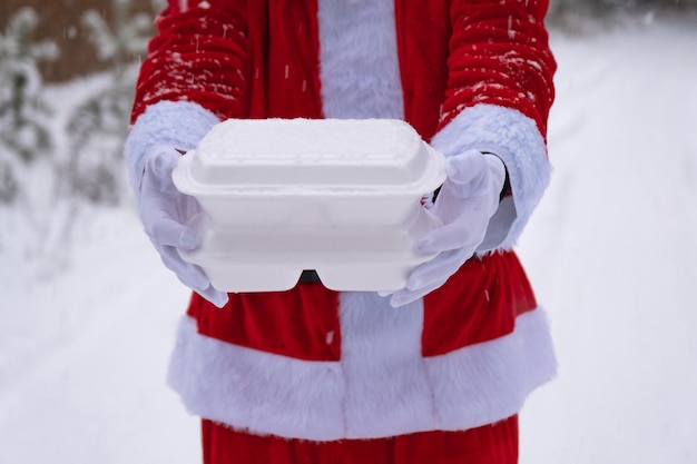 Food delivery service containers in hands of santa claus outdoor in snow christmas eve promotion readymade hot order disposable plastic box new year holidays catering copy space mock up