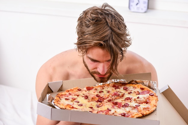 Servizio di consegna cibo ritratto di uomo muscoloso pigro che mangia pizza mentre è sdraiato su un letto a casa uomo