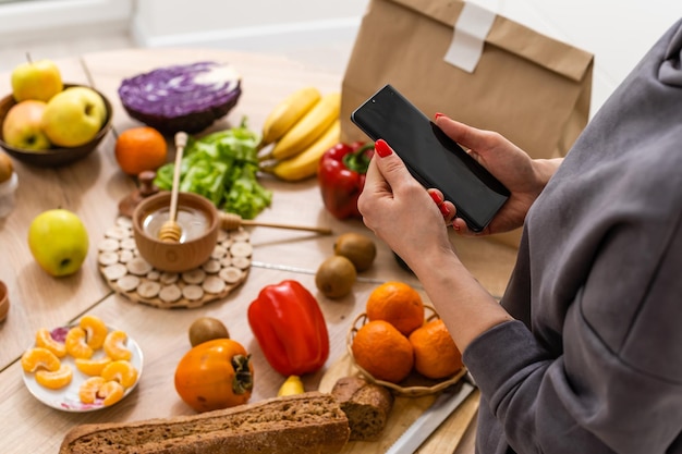 Foto servizio di consegna cibo - donna che tiene smartphone davanti alla scatola della spesa.