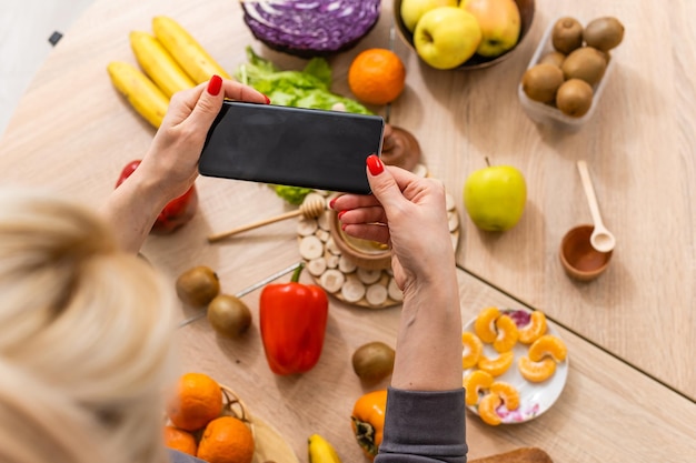 Foto servizio di consegna cibo - donna che tiene smartphone davanti alla consegna di cibo sano di verdure.