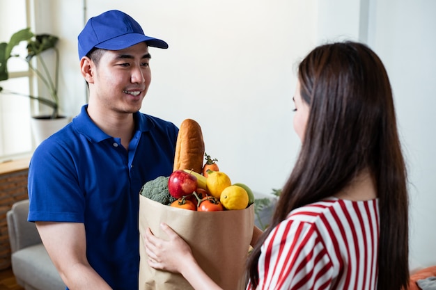 青い制服を着た配膳係が自宅の若い女性客に生鮮食品を届けました。