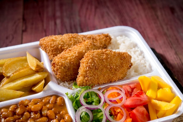 Food delivery, styrofoam lunch box with rice, beans, crispy\
fish fillet, potatoes and salad.