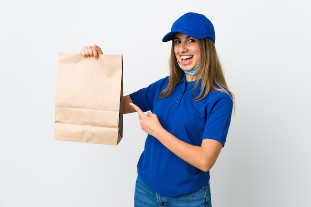 Food delivery woman and protecting from the coronavirus with a mask over isolated white wall and pointing it