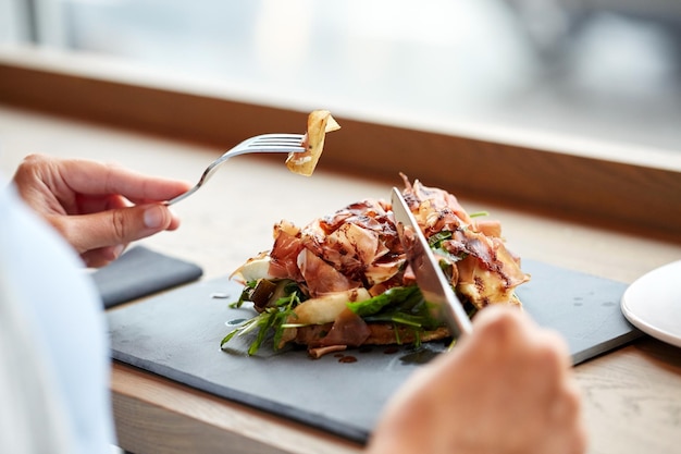 food, dinner and people concept - woman eating prosciutto ham salad on stone plate at restaurant