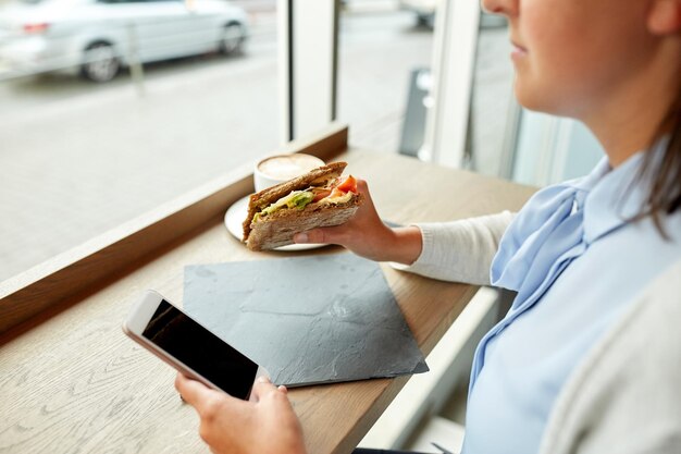 food, dinner, technology and people concept - woman with smartphone eating salmon panini sandwich with tomatoes and cheese at restaurant