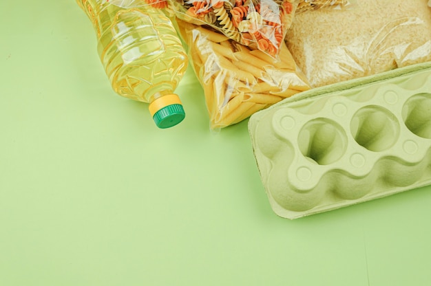Food donation, top view of a bottle of oil, chicken eggs, canned food, pasta, cookies isolated on a green background. Copy space