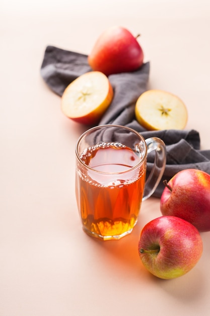 Еда и напитки, концепция осеннего падения урожая. Свежий органический яблочный сок в кружке со спелыми фруктами на модном розовом коралловом фоне. Копировать пространство