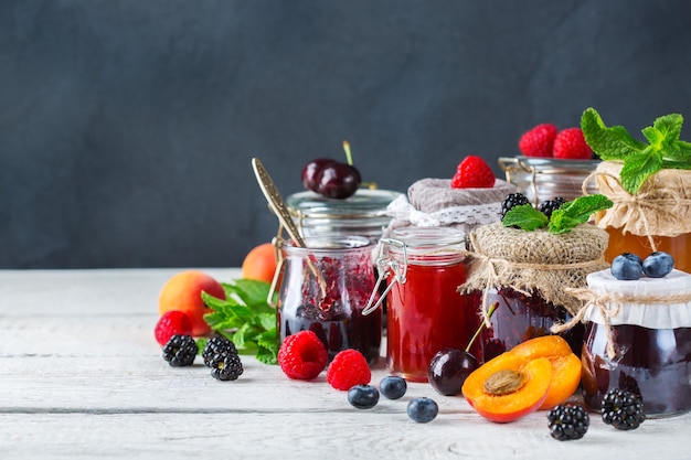 음식과 음료, 수확 여름 가을 개념. 나무 테이블에 있는 항아리에 다양한 계절 딸기와 과일 잼. 복사 공간 소박한 배경