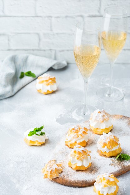 Food and drink, holidays concept. Delicious sweet homemade profiteroles with cream and glasses of champaigne on a modern kitchen table