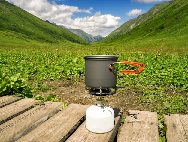 山の谷の背景にあるキャンプ用ガスストーブの調理鍋での食べ物や飲み物の準備