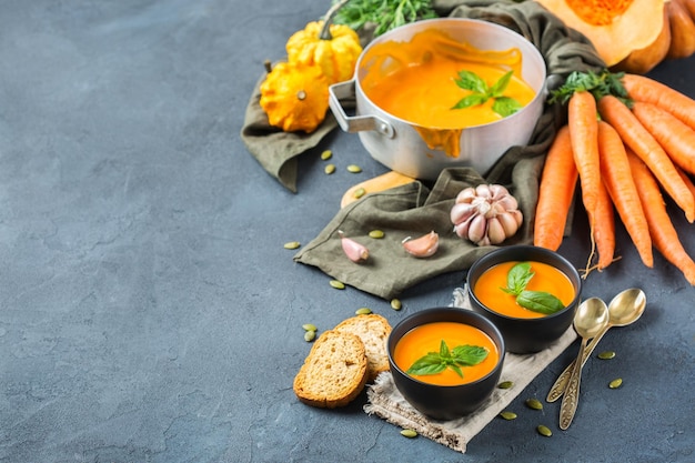 Food and drink still life diet and nutrition concept Seasonal fall autumn roasted orange pumpkin carrot soup with ingredients on a rustic wooden table Copy space cozy kitchen background