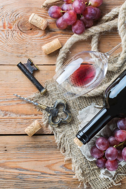 Food and drink still life holidays seasonal harvesting fall concept Bottle corkscrew corks glass of red wine and grapes on a rustic wooden table Top view flat lay