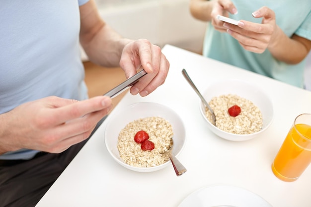 food, eating, people, technology and healthy food concept - close up of couple having breakfast and texting on smartphones at home