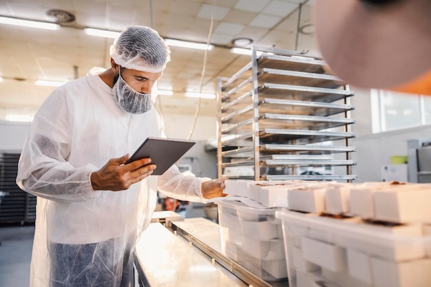 Супервайзер пищевой фабрики использует планшет и оценивает качество еды