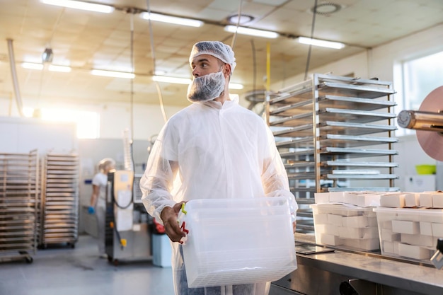 A food factory worker in a white sterile uniform is relocating plastic containers