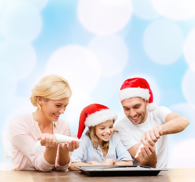 food, family, christmas, hapiness and people concept - smiling family in santa helper hats decorating cookies with glaze