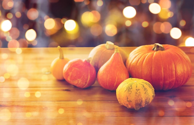 Food, halloween, harvest, season and autumn concept - close up of pumpkins on wooden table over holidays lights
