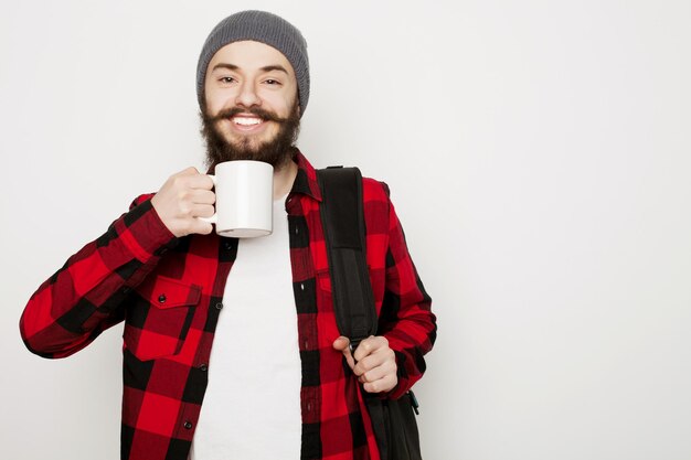 Concetto di cibo, felicità e persone: giovane uomo barbuto con una tazza di caffè su sfondo grigio